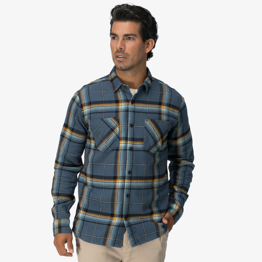 Man wearing a blue plaid Dyson Flannel Shirt with front pockets, modeled for casual beach-inspired comfort apparel.
