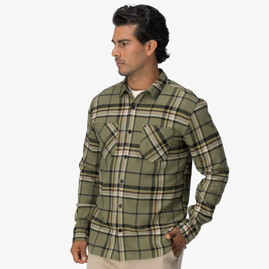 Man wearing a green plaid Dyson Flannel Shirt facing left with hands in pockets, showcasing front and sleeves.