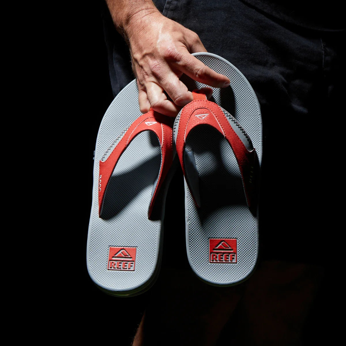Pair of Fanning Pregame sandals held by hand, top view showing grey footbeds and red straps, beach-ready comfort style facing up.