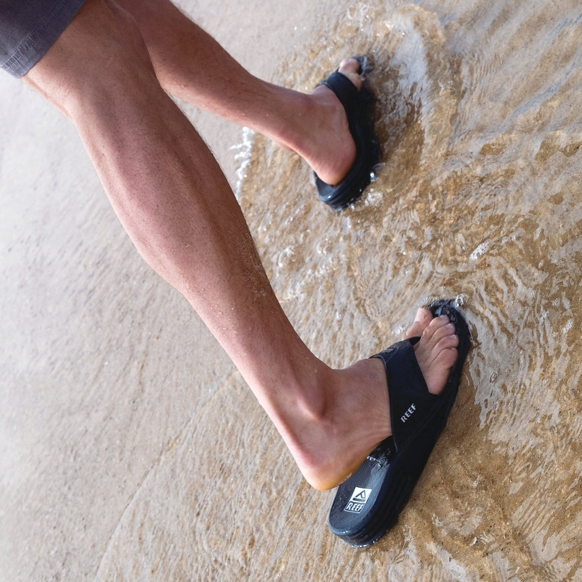 Fanning H2O facing right on feet stepping into shallow water, men's black water-friendly sandals with arch support and cushioned footbed