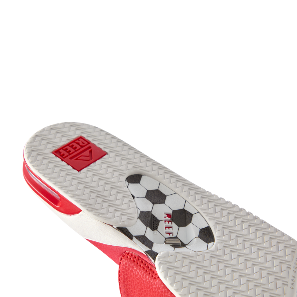 Fanning Slide facing left showing hexagonal tread, red detail, soccer ball graphic with REEF logo on water-friendly sole
