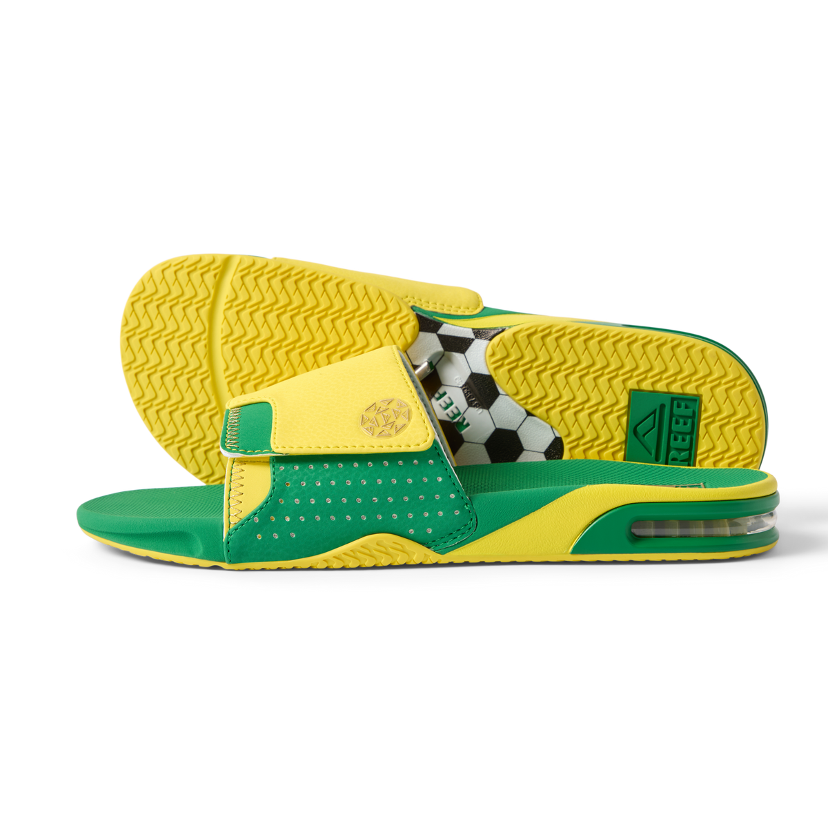 Pair of Fanning Slide sandals facing right and sole up, men's green and yellow water-friendly slides with cushioned EVA footbed and soccer ball graphic underfoot.