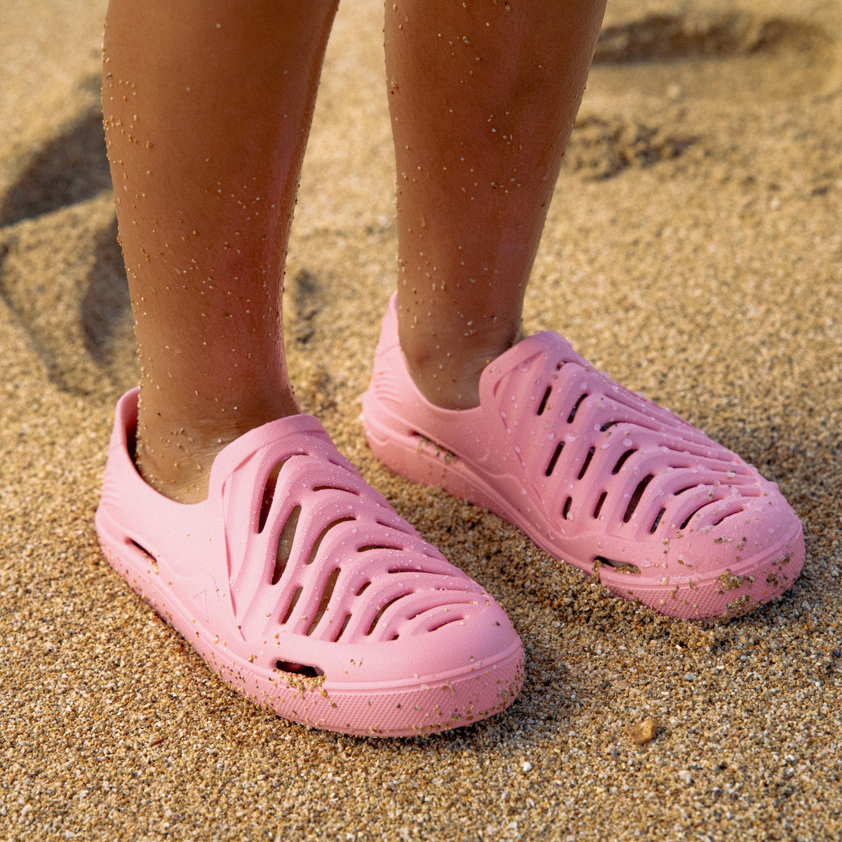 Kids Reef Sandbar coral clogs facing forward on sandy beach, water-friendly and comfort-focused footwear for kids.