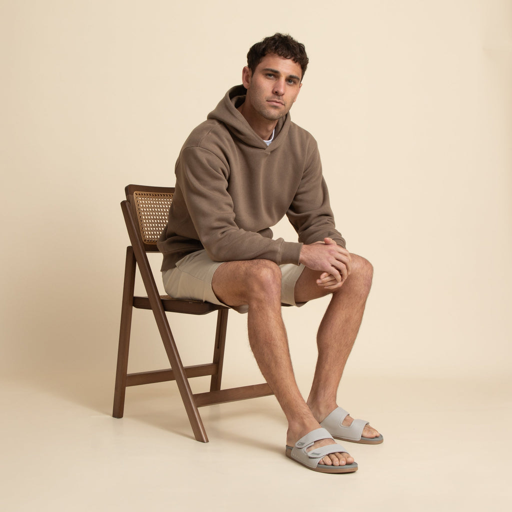 Man sitting on wooden chair wearing Phantom Tradewind sandals facing forward, showcasing soft-rebound cushioning and arch support.