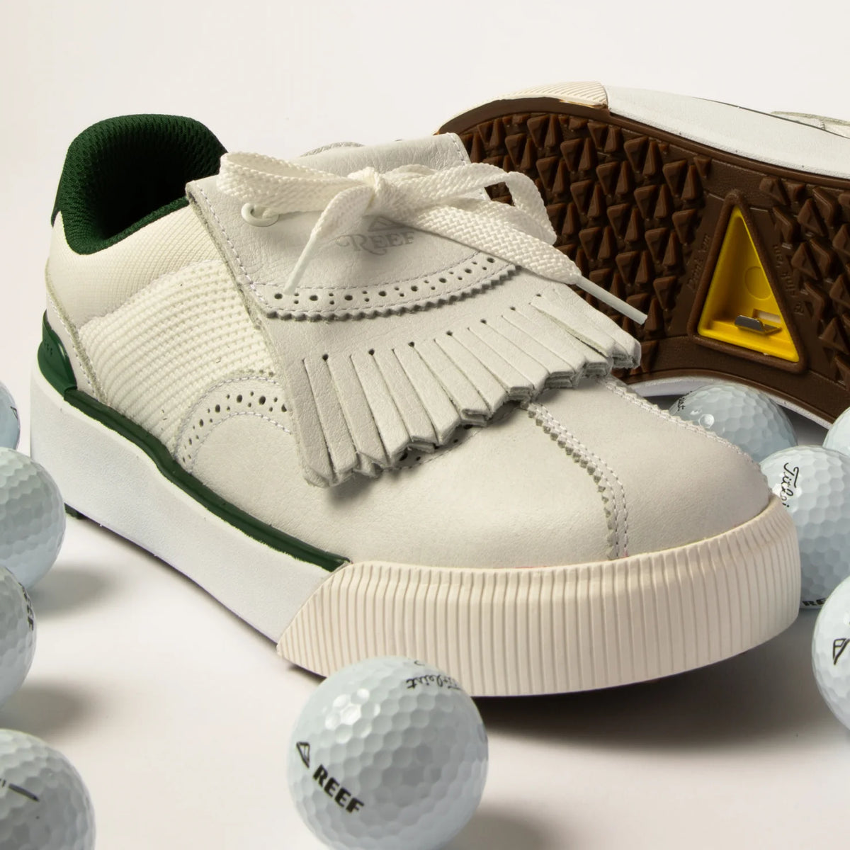 Onshore Pebble men's sneaker facing left, close-up of toe and fringe detail with golf balls on white surface.