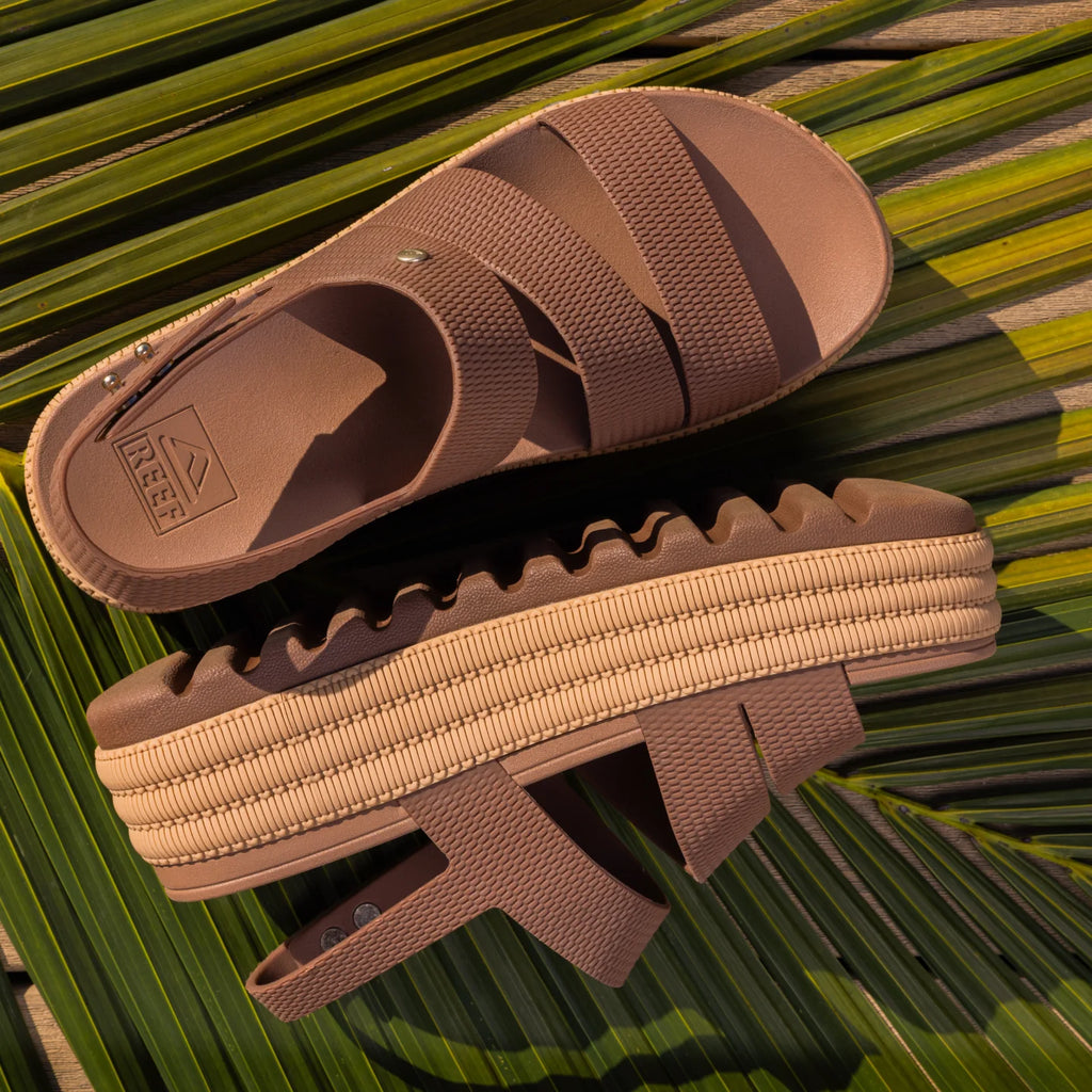 Pair of brown Water Vista Higher 2 sandals facing right, showing side and top views with platform sole on palm leaves.