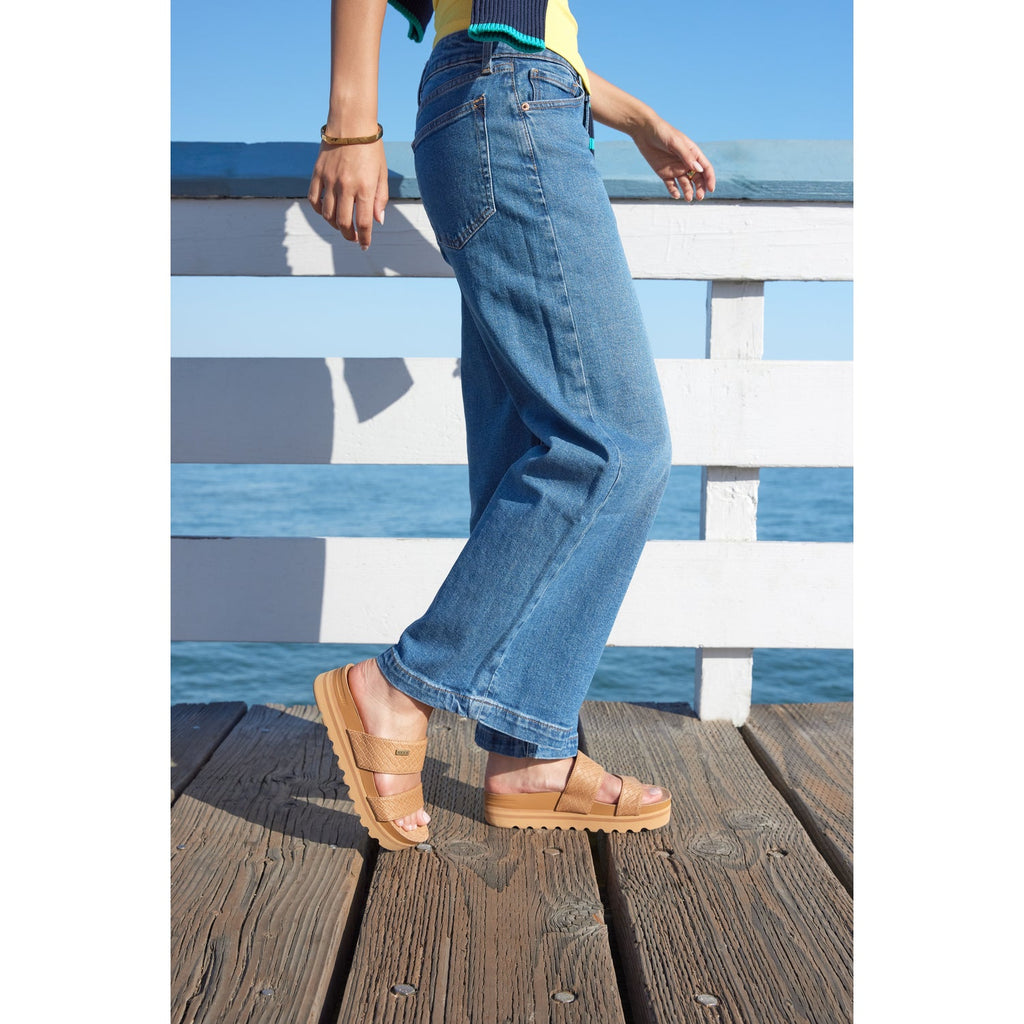 Side view of women's Cushion Vista Hi tan sandals on a wooden pier, highlighting comfort and beach-inspired design.