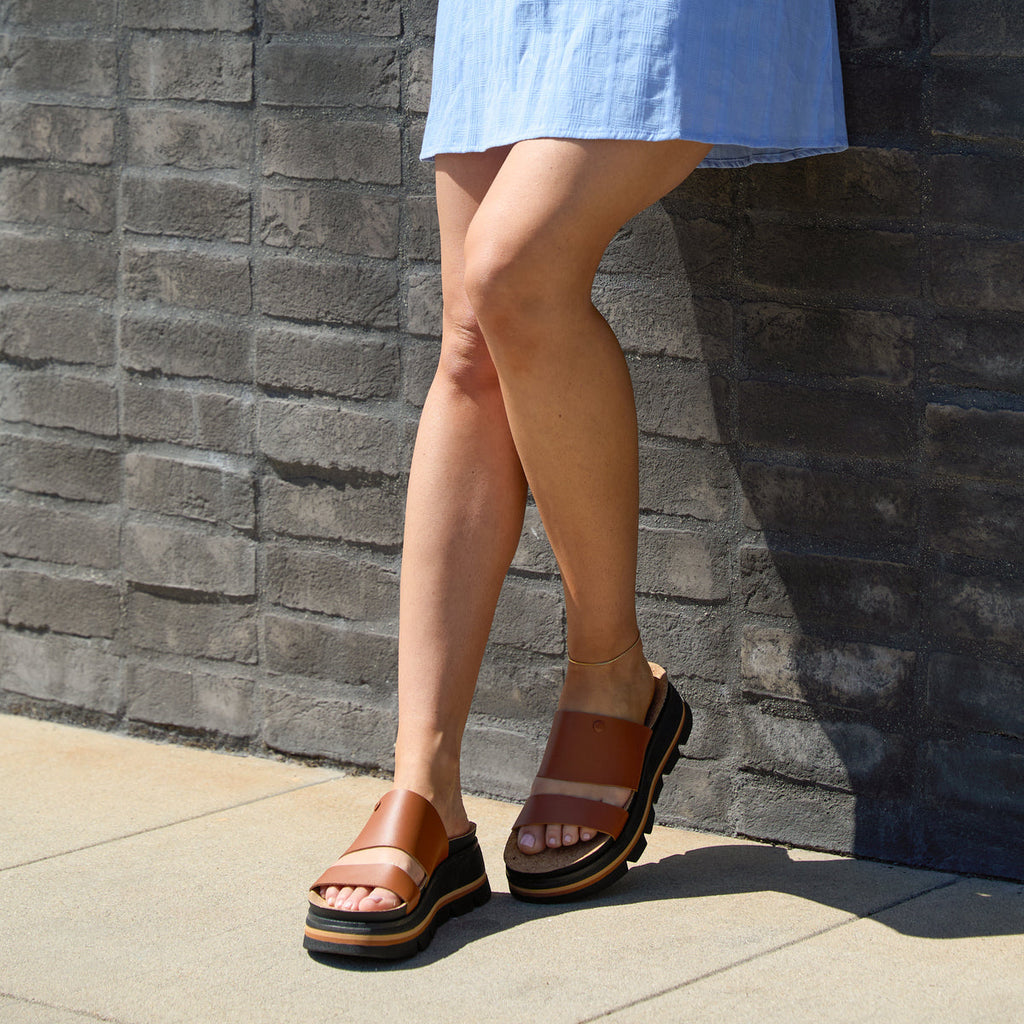 Woman wearing brown Vista Luxe Siaa sandals facing forward, showing platform sole and anatomical arch support outdoors.
