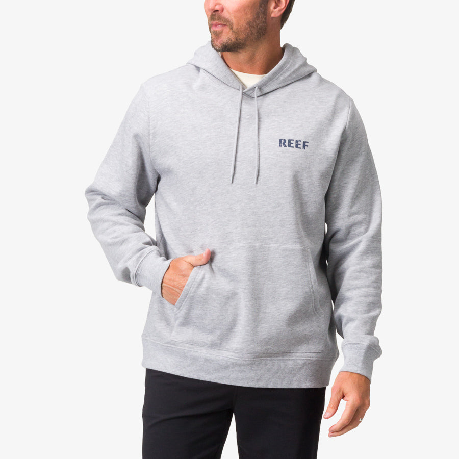 Male model wearing a Heather Grey Wellie Too Hoodie facing forward with hand in front pocket, beach-inspired comfort apparel.